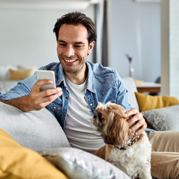 Man looking at his phone while petting a dog