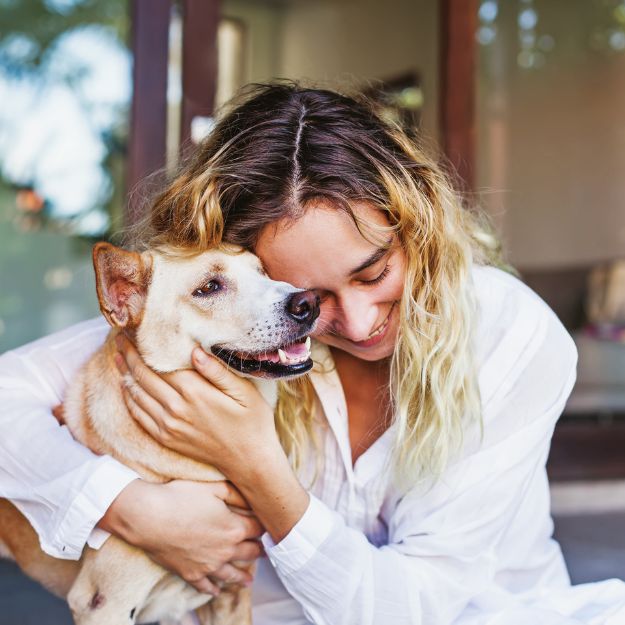 A person in a white shirt is embracing a tan dog with their eyes closed in affection